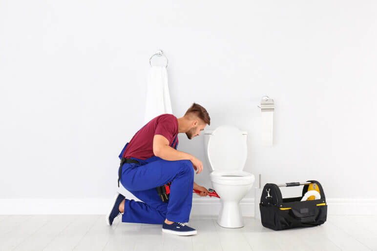 男人弯腰在白色厕所和工具箱旁边
