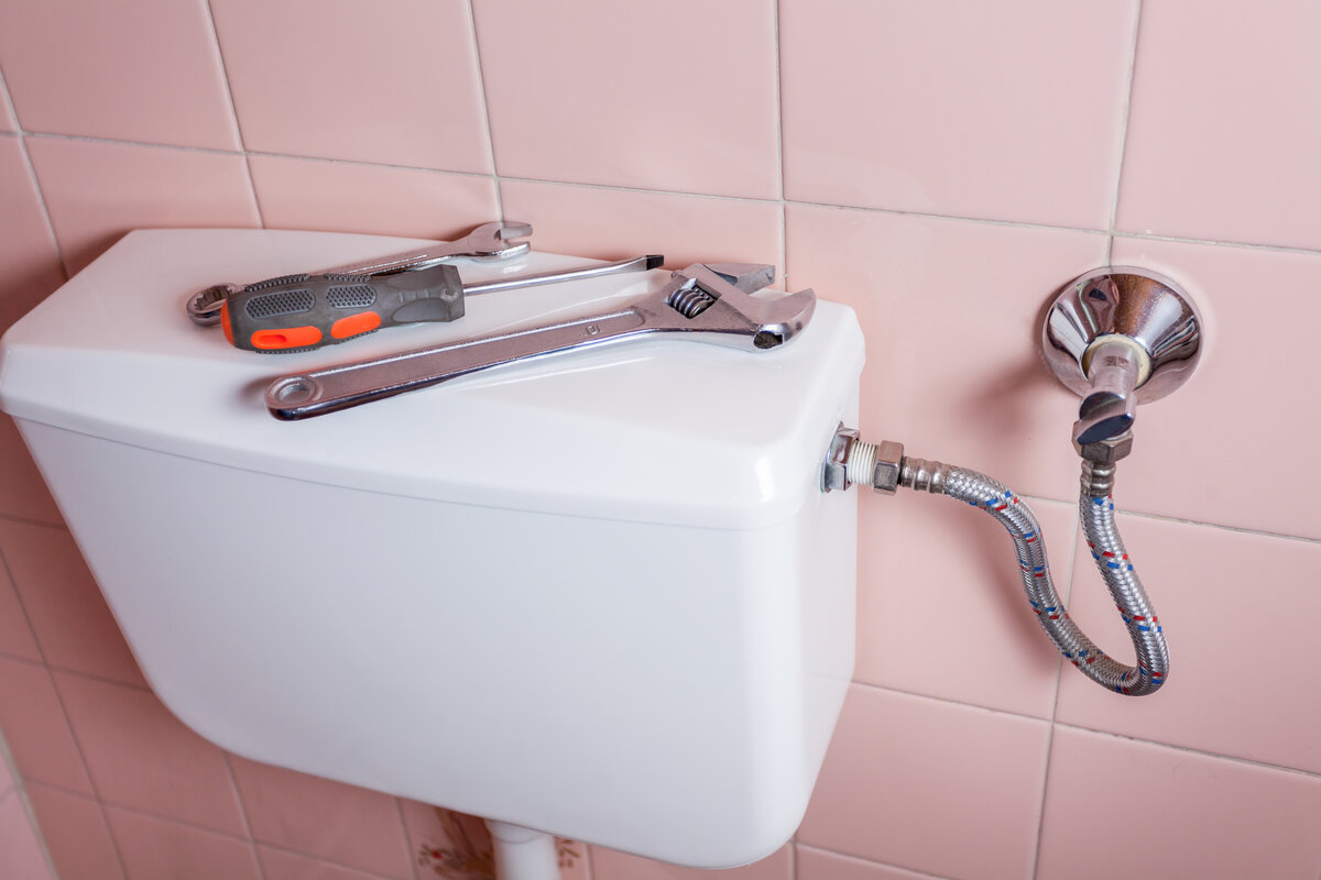 White toilet tank in front of pink tile wall with tools on top of the lid